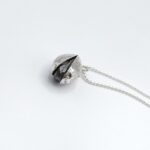 a silver bell necklace on a white surface