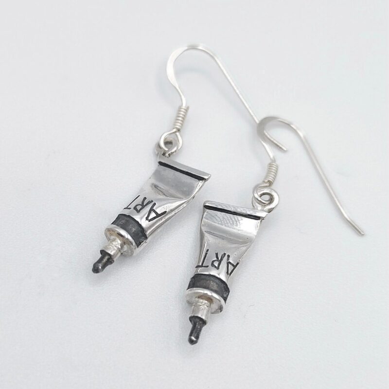 a pair of earrings with a tube of paint